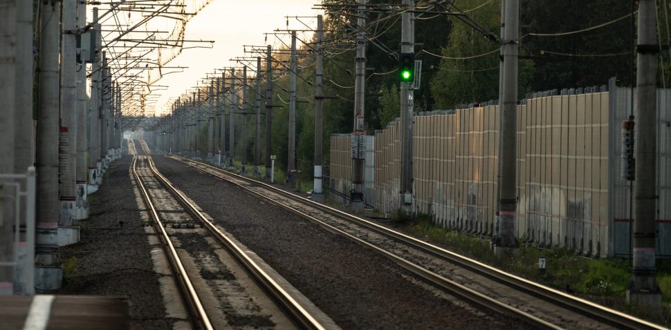 Empty railway tracks at sunset, forest on background. Perspective of electrified high-speed railroad